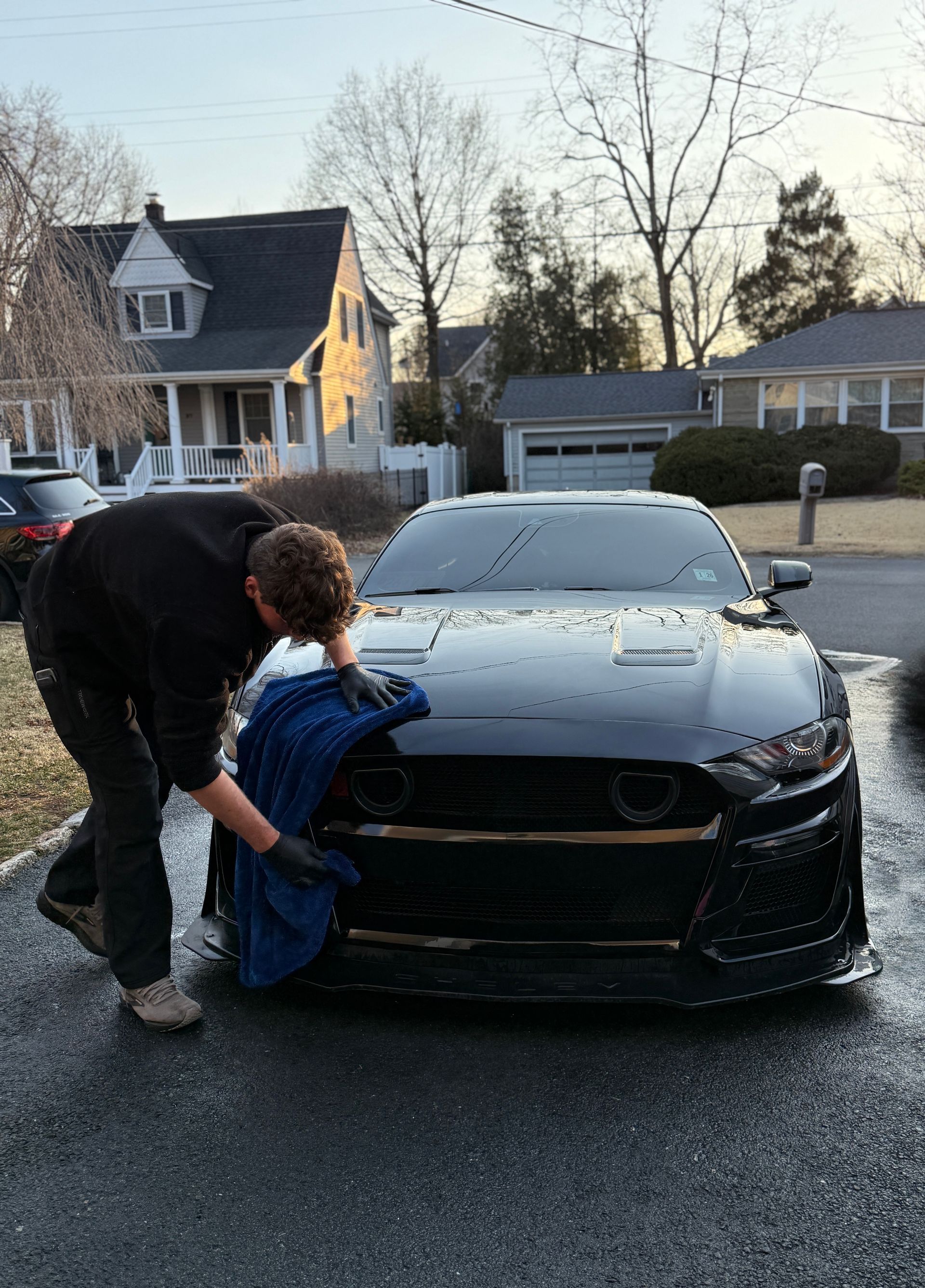 A man is washing a black mustang in a driveway.