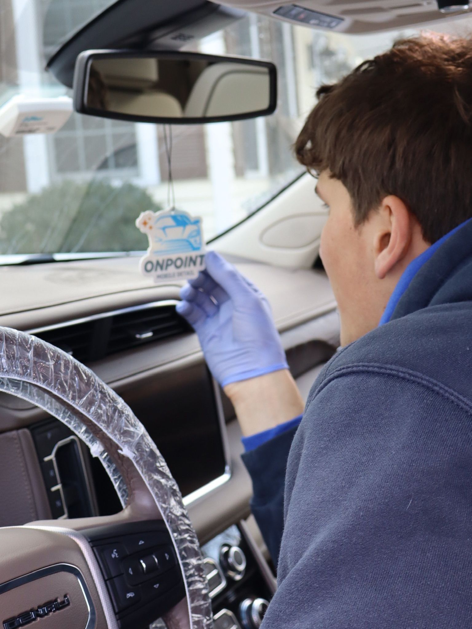 A man wearing blue gloves is holding a car air freshener in his hand