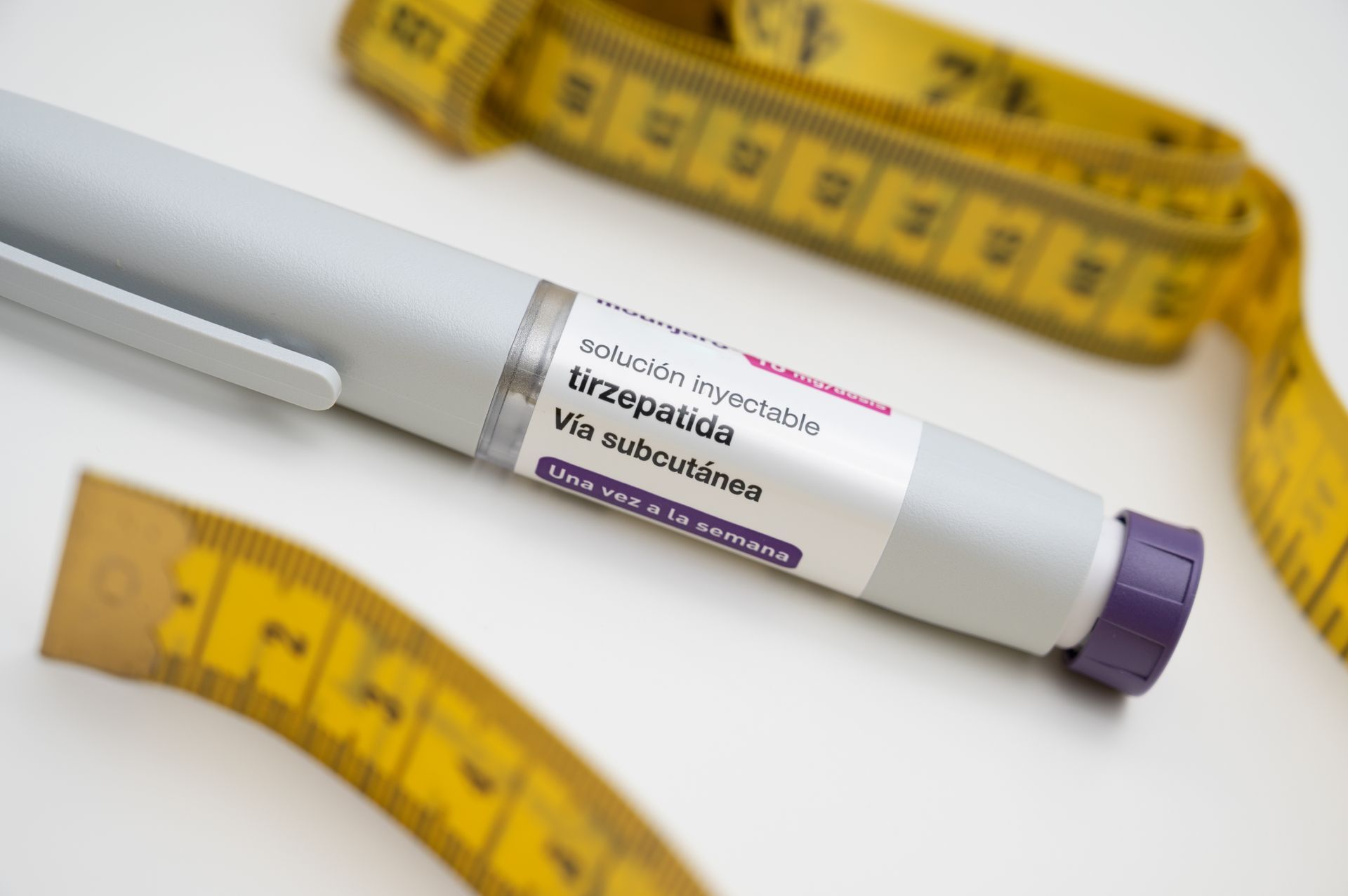White insulin pen with purple cap beside yellow measuring tape on a white background