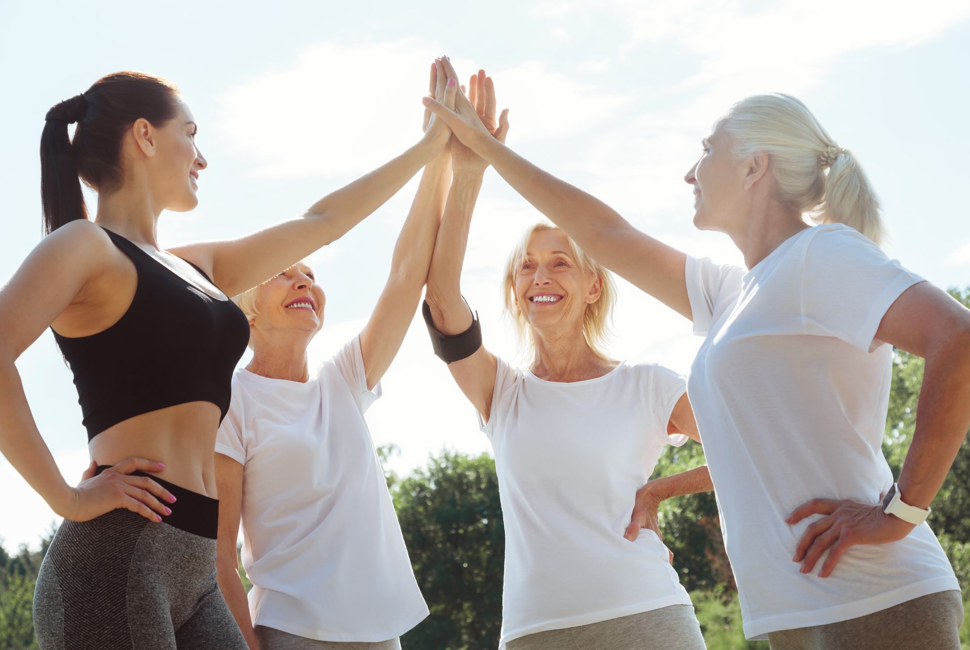 Four people in workout clothes high-fiving outdoors.