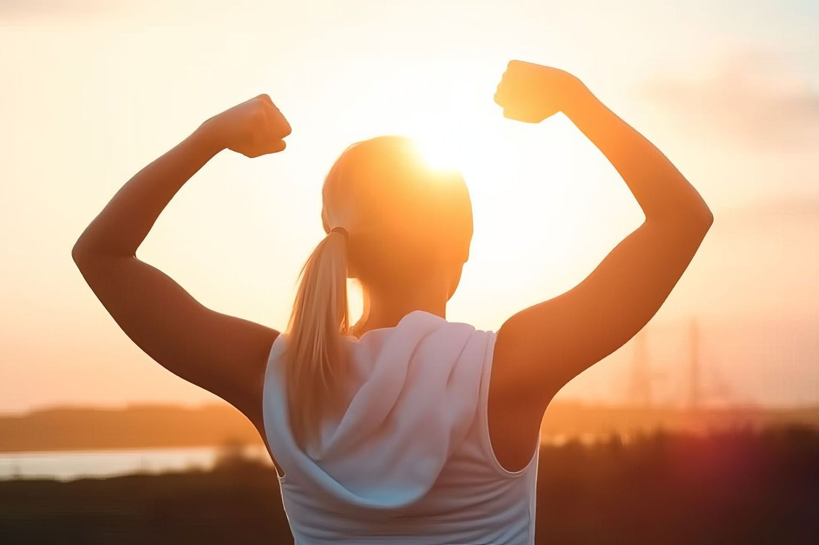 Woman with arms raised in victory pose, silhouetted against a bright sunset.