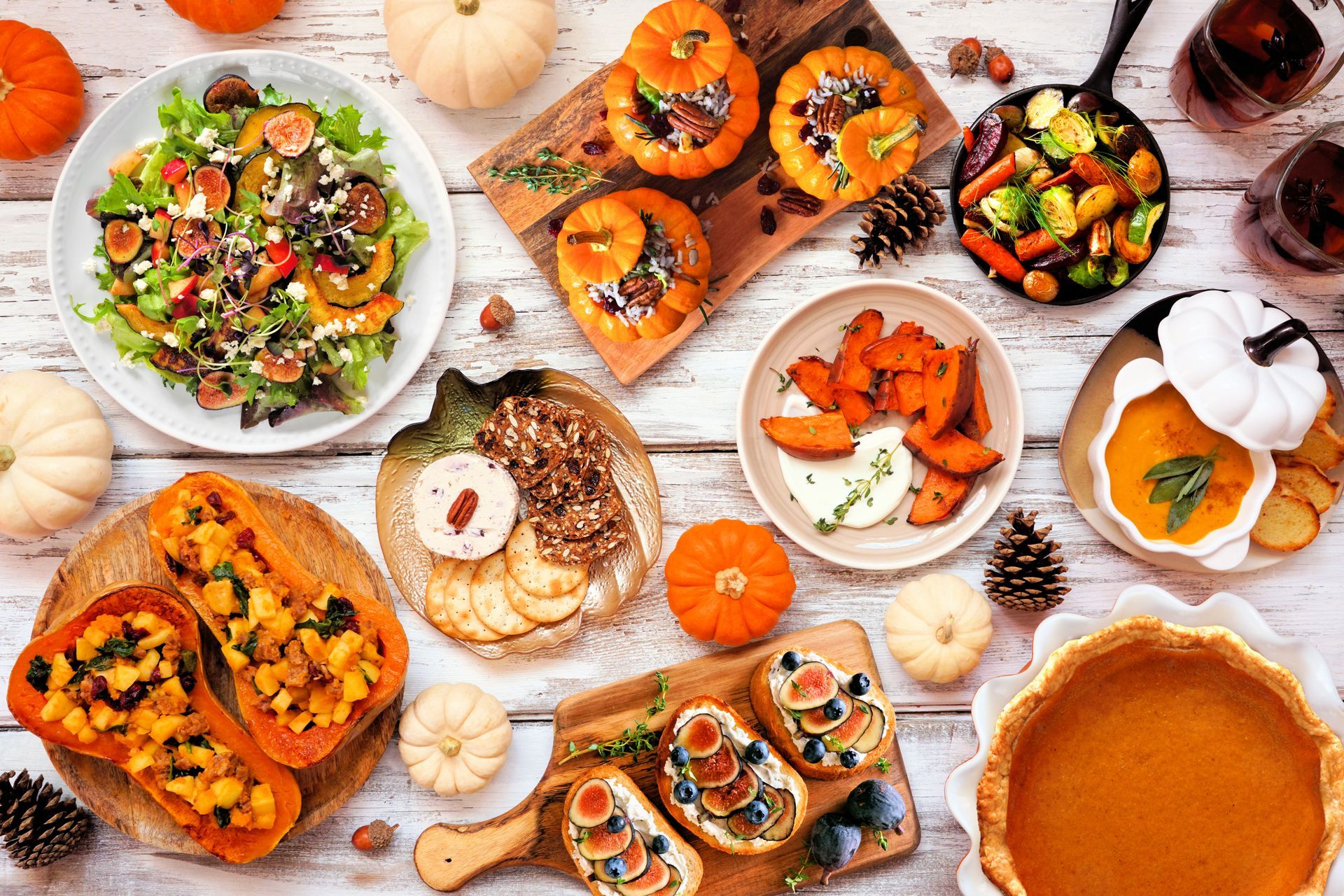 Autumn table spread with pumpkin dishes, salad, pastries, and pie on a white wooden surface