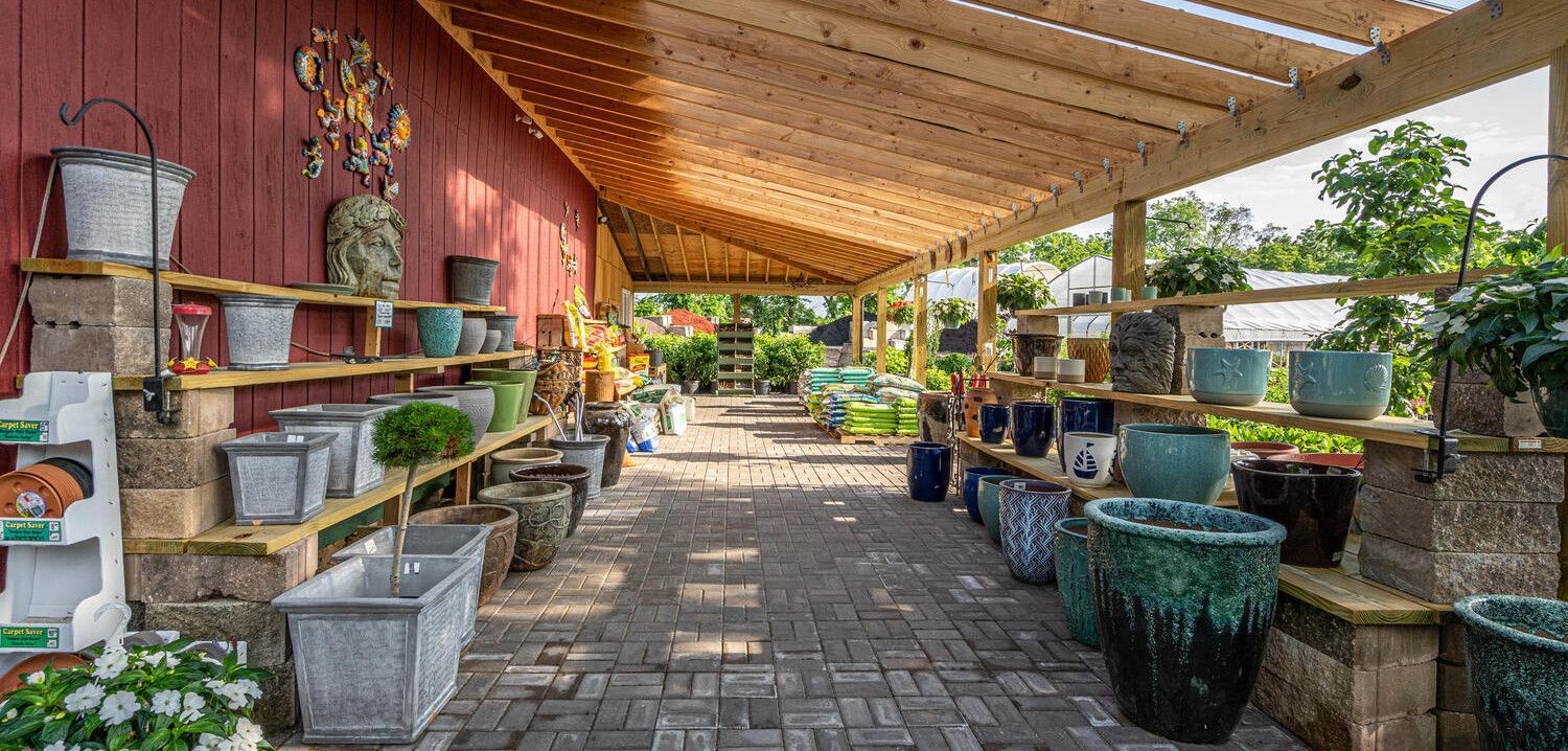 Covered outdoor garden center with potted plants, shelves, and brick flooring under a wooden roof