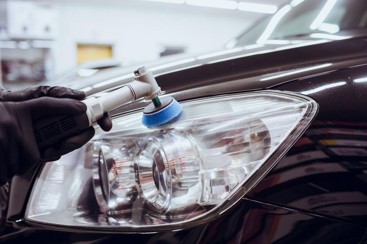 A person is polishing the headlights of a car.