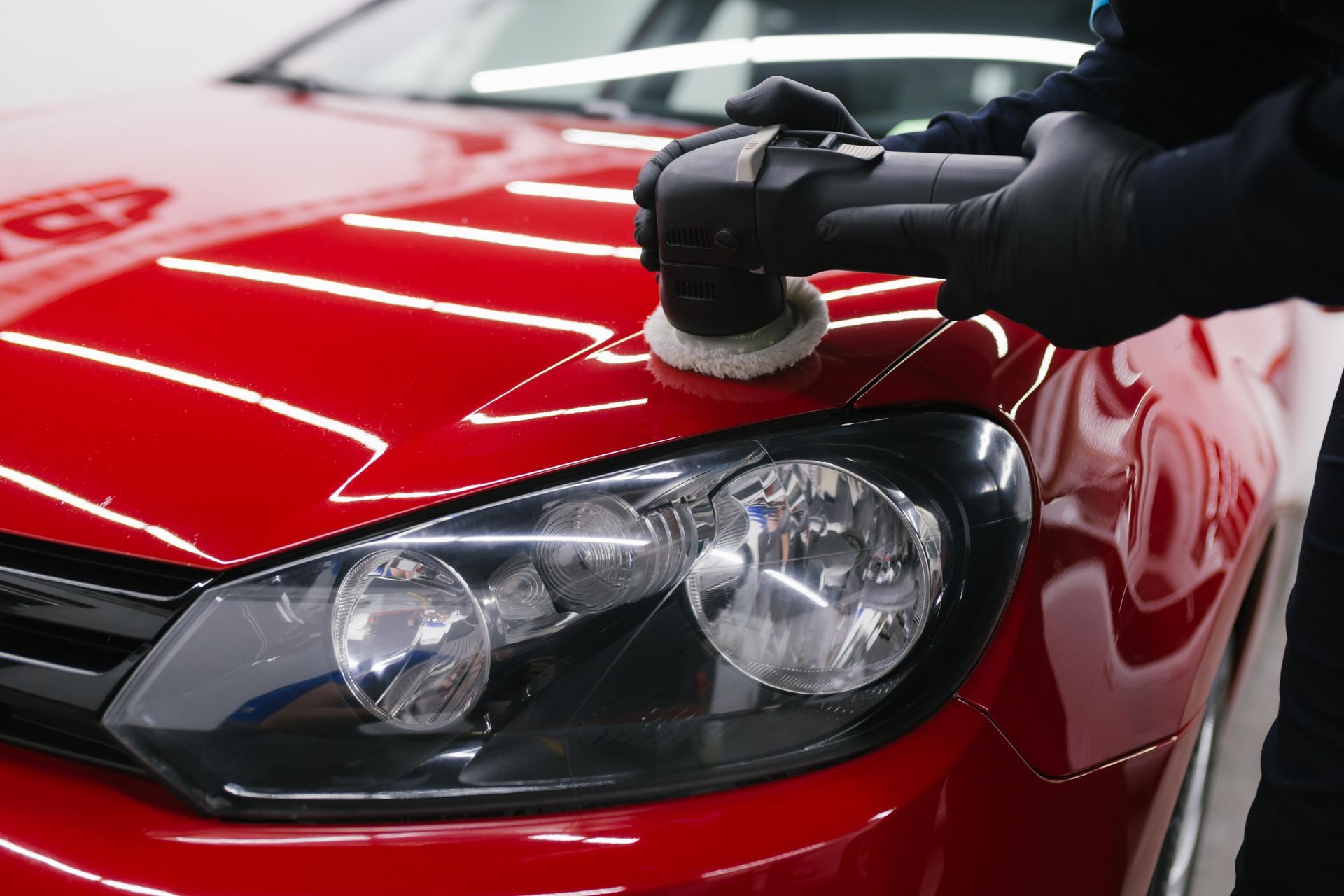 A gloved hand polishing the red hood of a car with a buffer