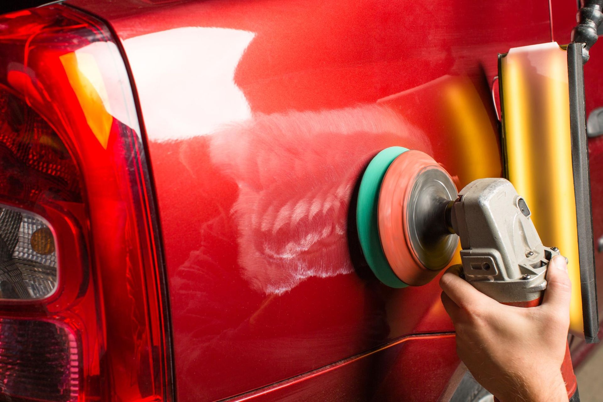 A person is polishing a red car with a machine.
