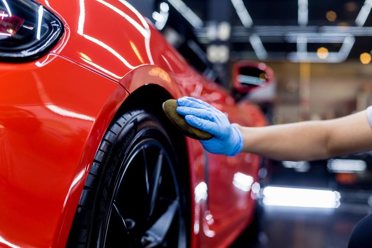 A person is polishing a red car with a sponge.