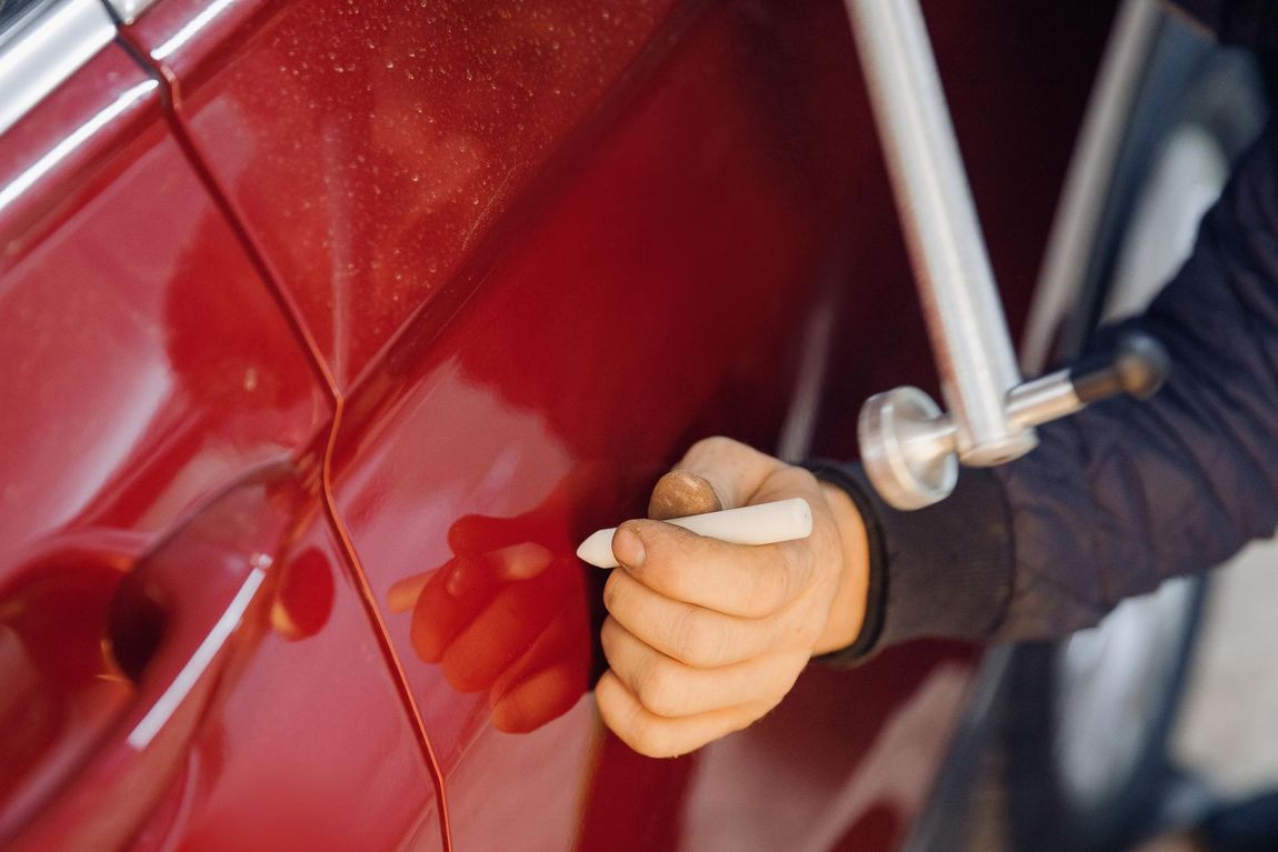A person is using a tool to fix a scratch on a red car.