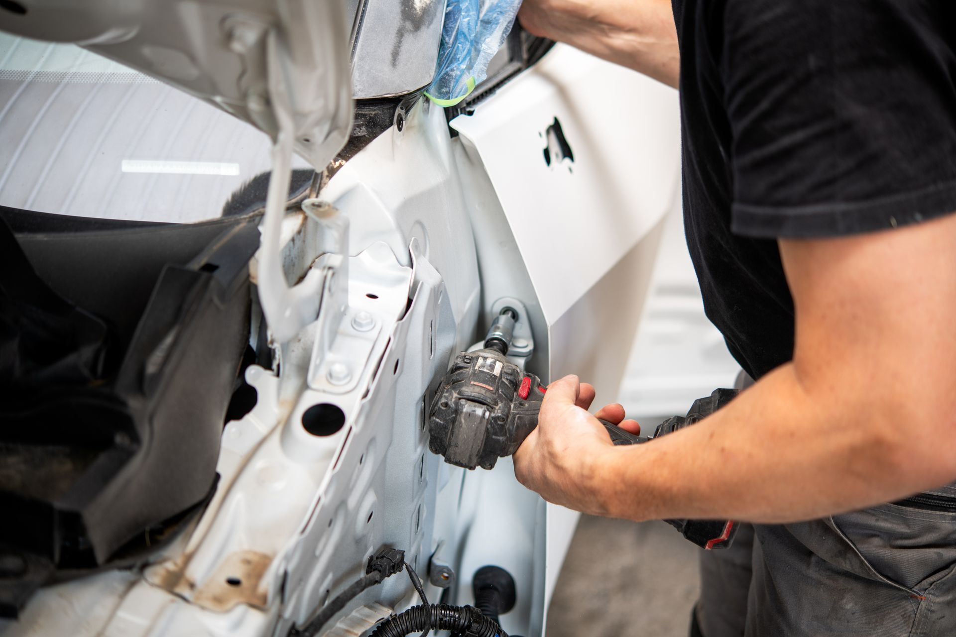 Mechanic repairing a white car’s damaged side panel with tools in a garage