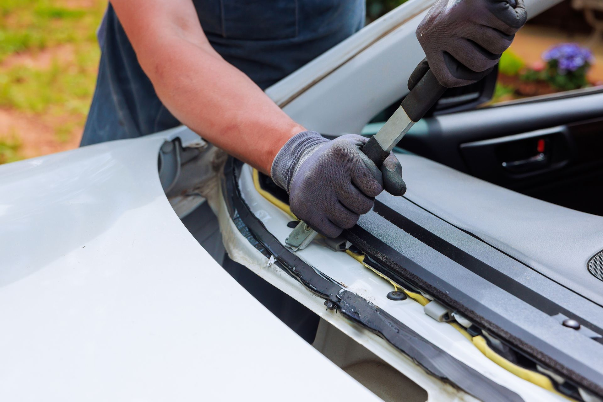 Person using a pry tool to remove trim from a white car windshield area
