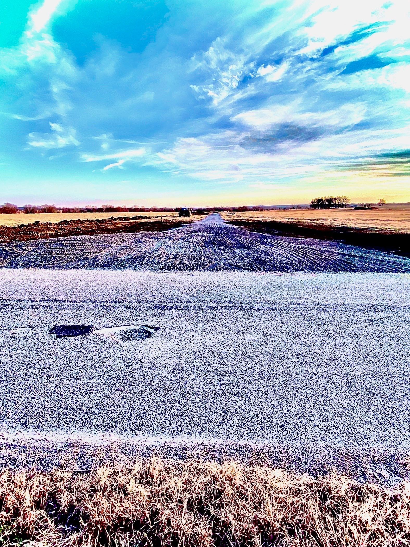 A wide, flat landscape under a vibrant blue sky, with a textured, silvery field stretching toward the horizon.