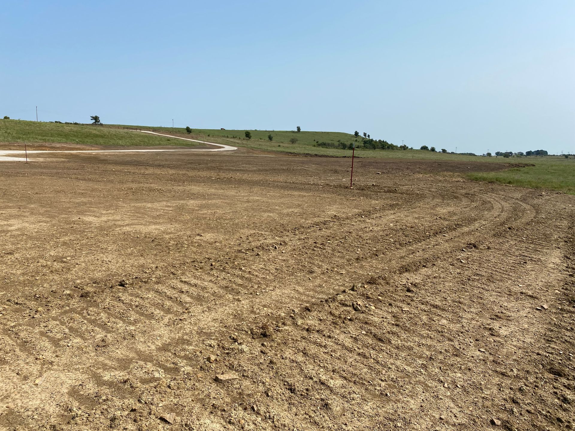 A freshly cleared, barren field with tire tracks and a single metal post under a clear blue sky.