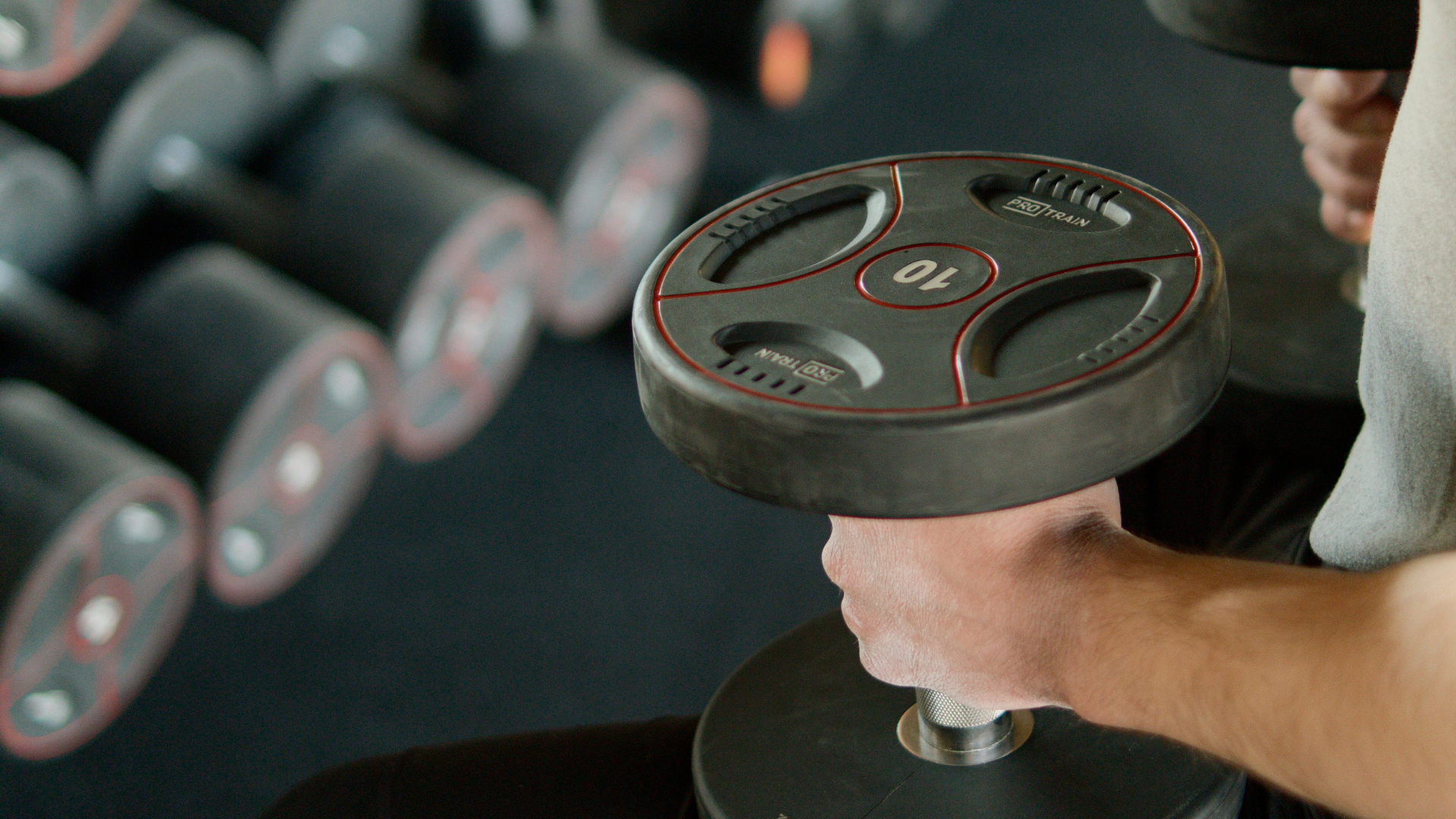 Person lifting a dumbbell in a gym, with more weights blurred in the background