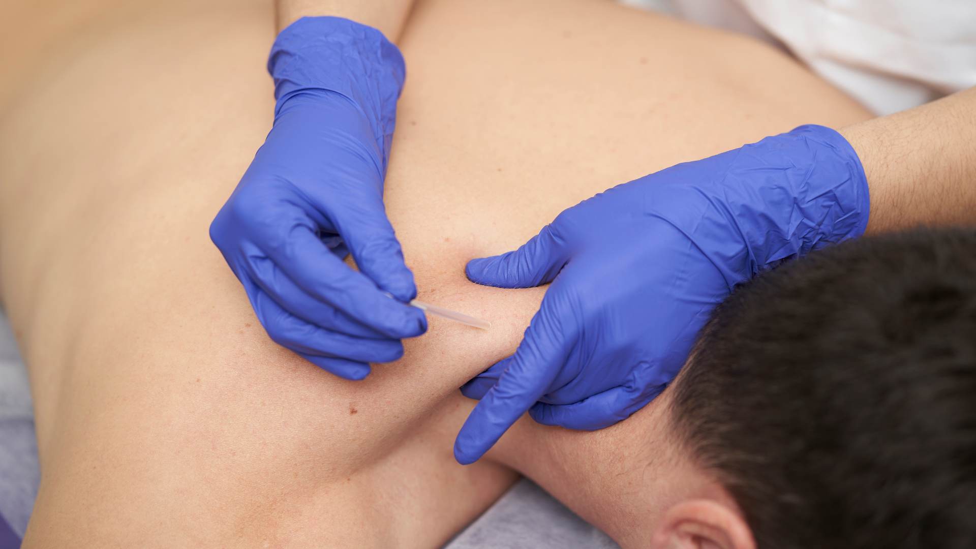 Gloved hands performing a medical back examination on a patient lying face down