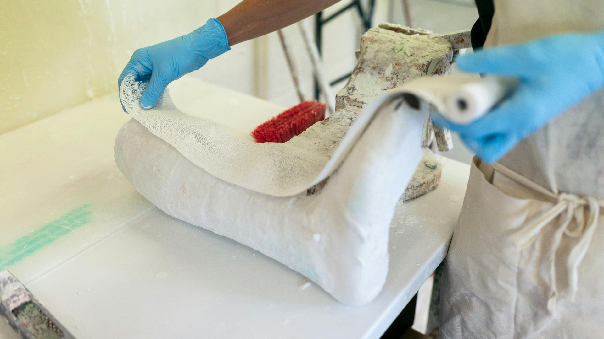 Gloved worker cleaning a white sofa with a brush in a workshop