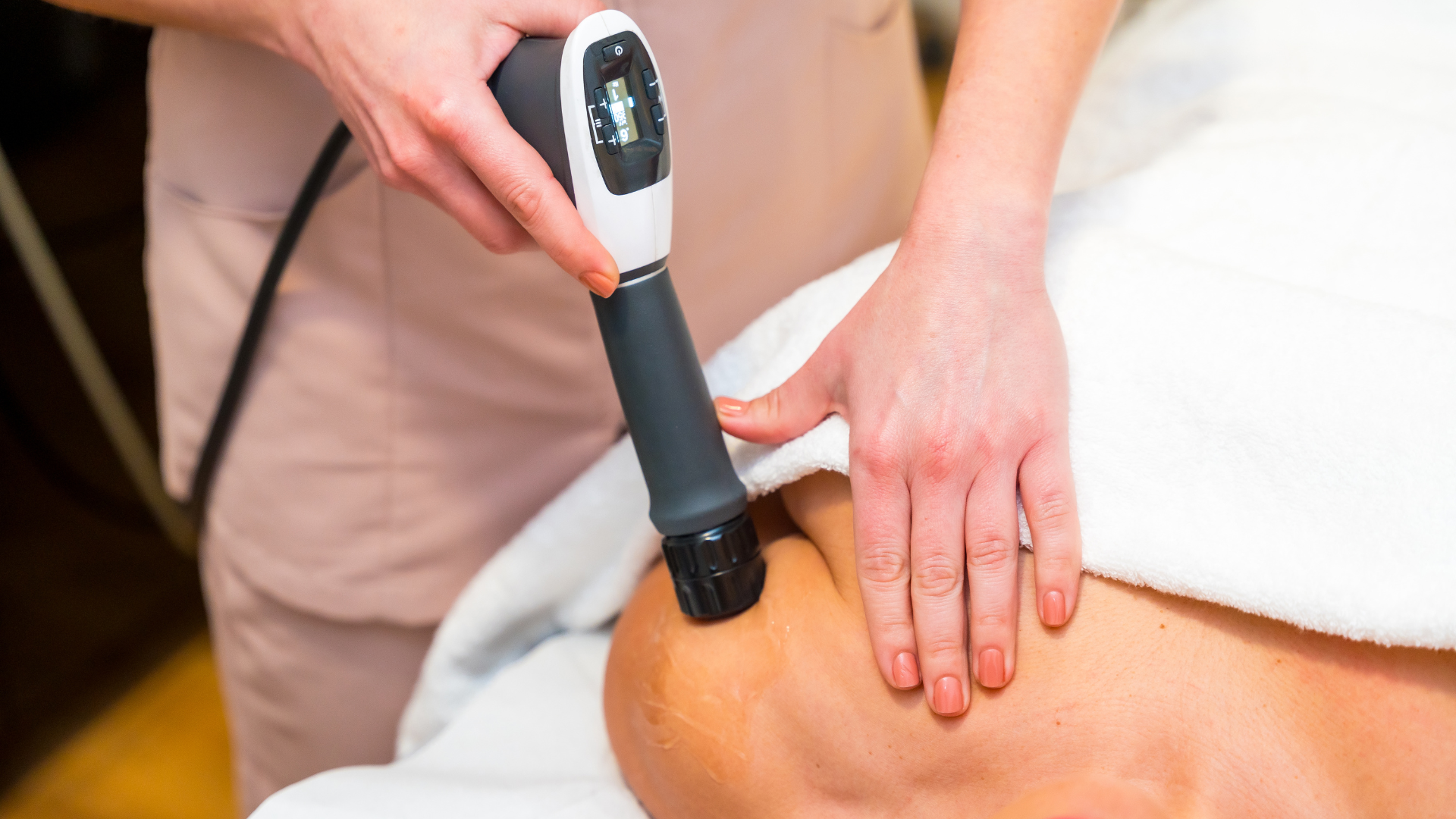 Massage therapist using a handheld device on a person's bare back under a white towel
