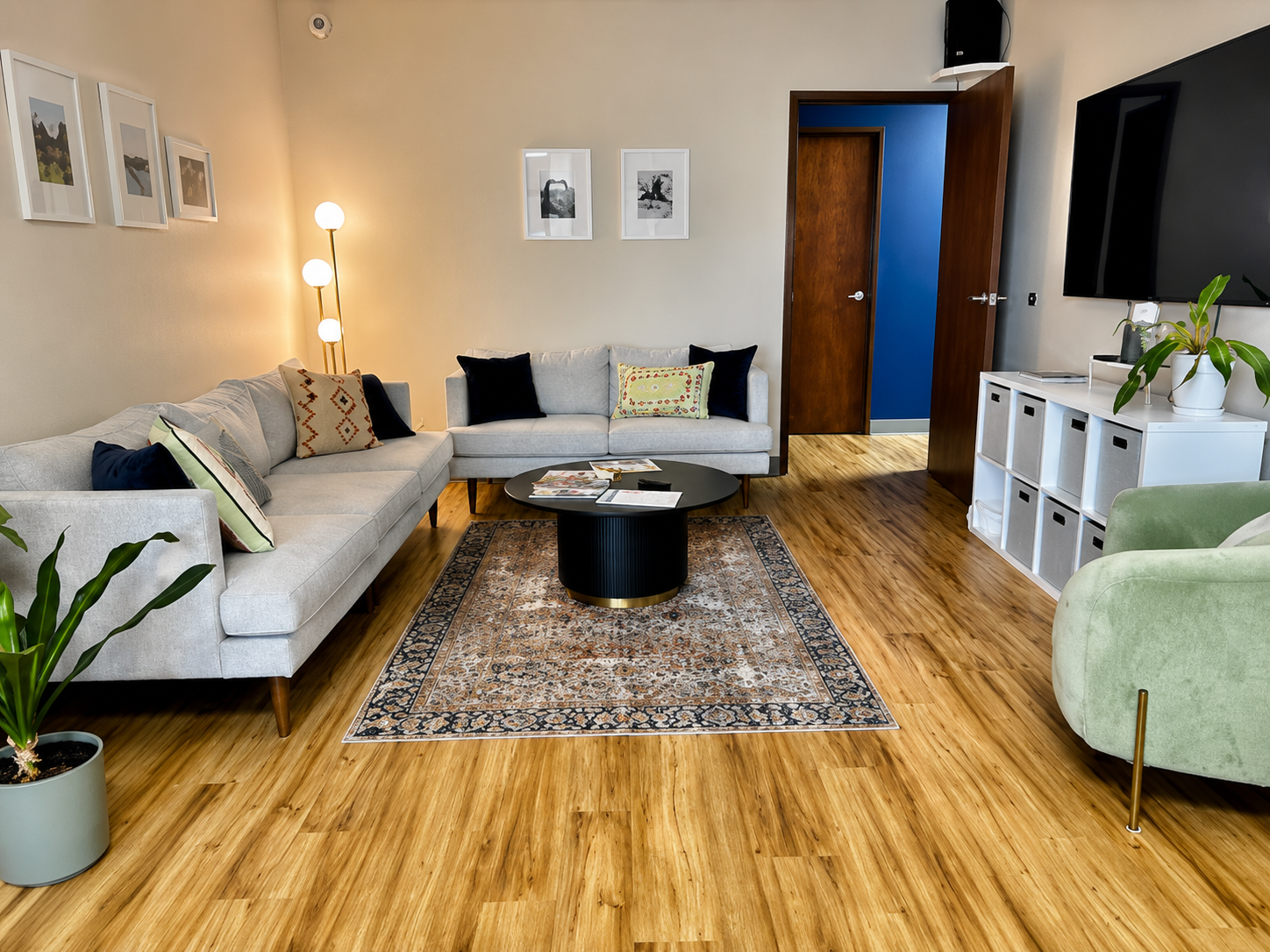 Modern living room with gray sofa, green armchair, wood floors, rug, and TV console