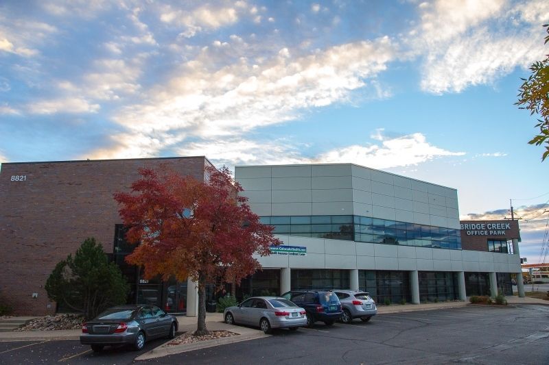 Modern office building with parked cars and a red tree under a cloudy sky