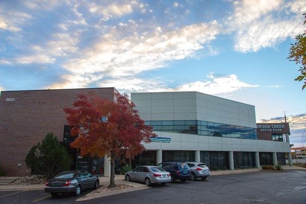 Modern office building with parked cars and a red tree under a cloudy sky