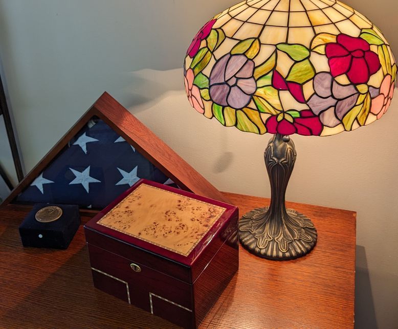 Tiffany-style lamp beside folded American flag and small wooden keepsake boxes on a table