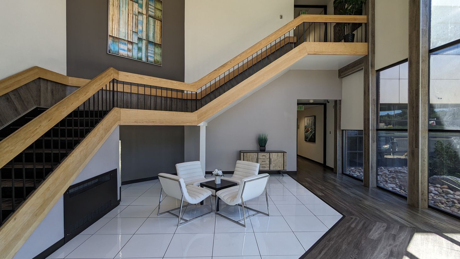 Modern lobby with staircase, white seating, and large windows overlooking greenery