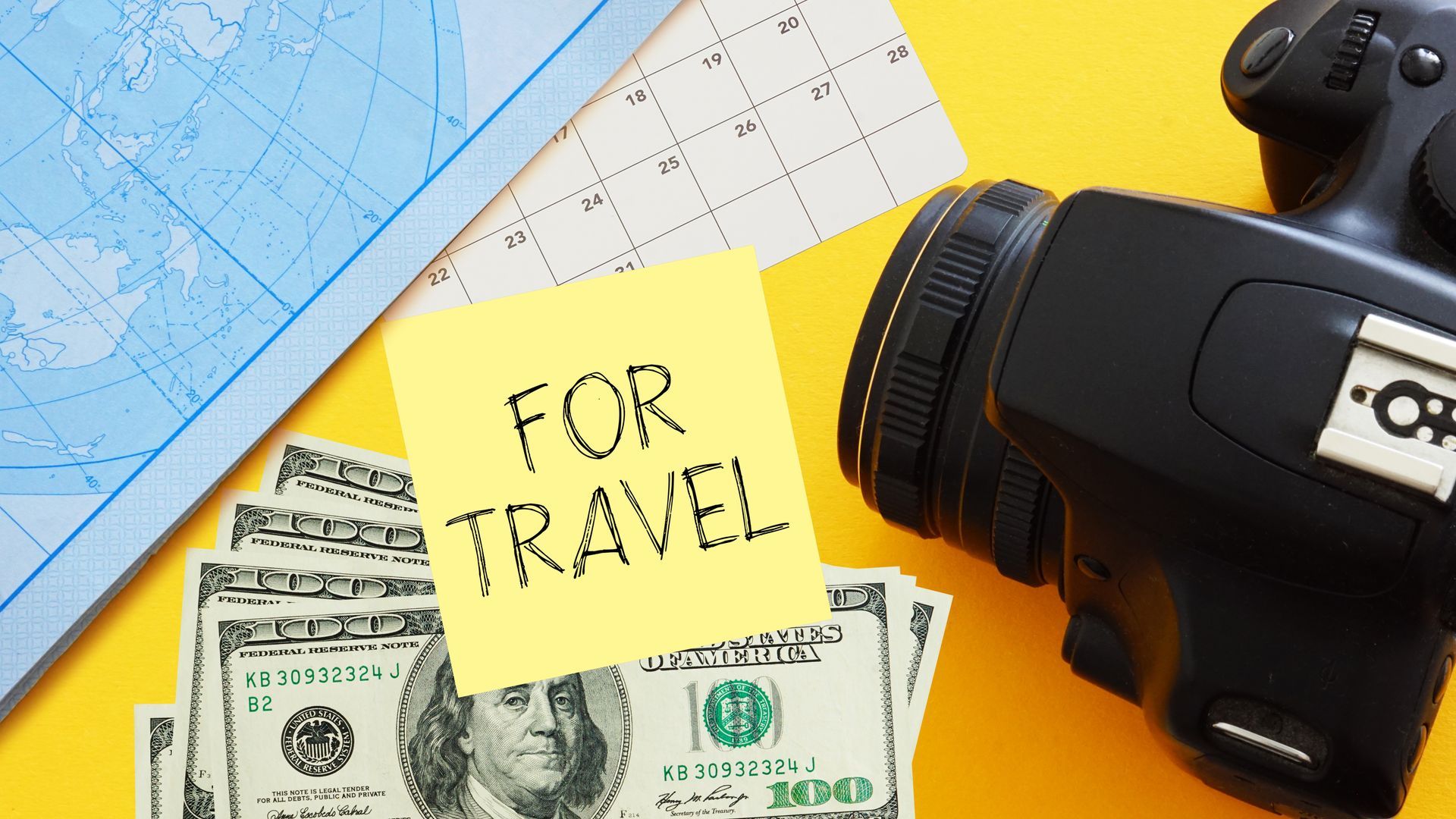 Travel planning with map, dollar bills, a yellow “For Travel” note, and a camera lens on a yellow-blue background