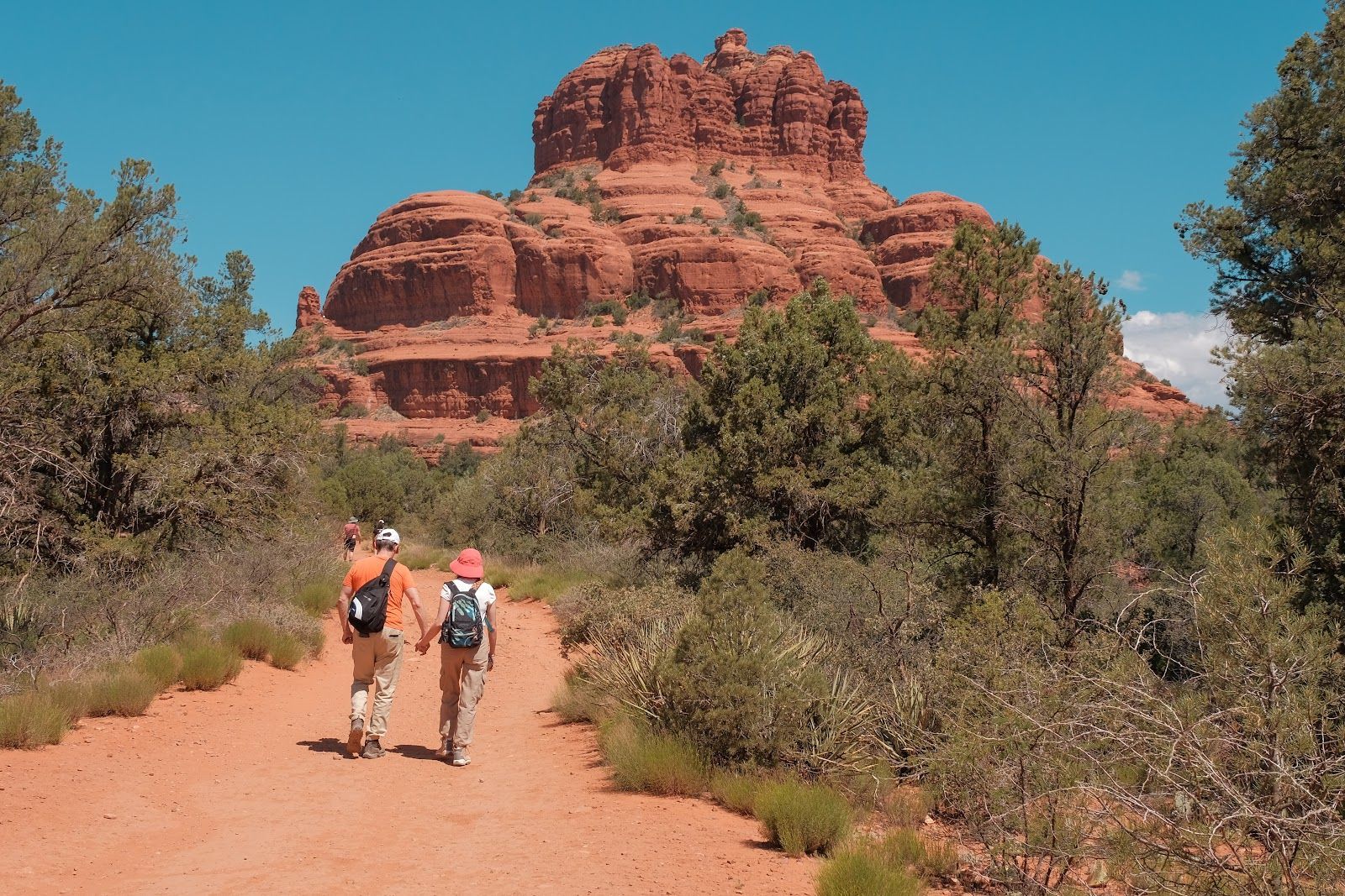 Couple walking hand in hand toward Bell Rock in Sedona, Arizona, on the Bell Rock Pathway