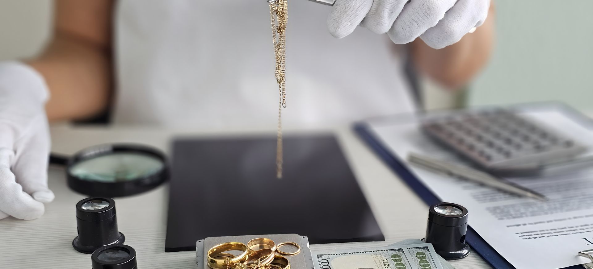 Gloved hands handling a gold jewelry chain over a display table with a calculator nearby