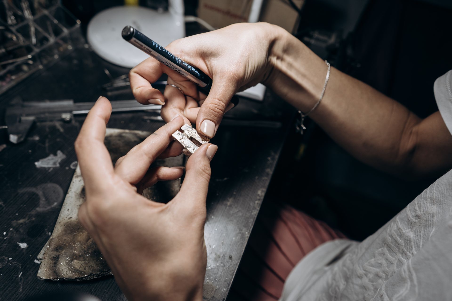 Hands preparing a small item with foil and a pen on a cluttered work surface. Hands preparing a small item with foil and a pen on a cluttered work surface.
