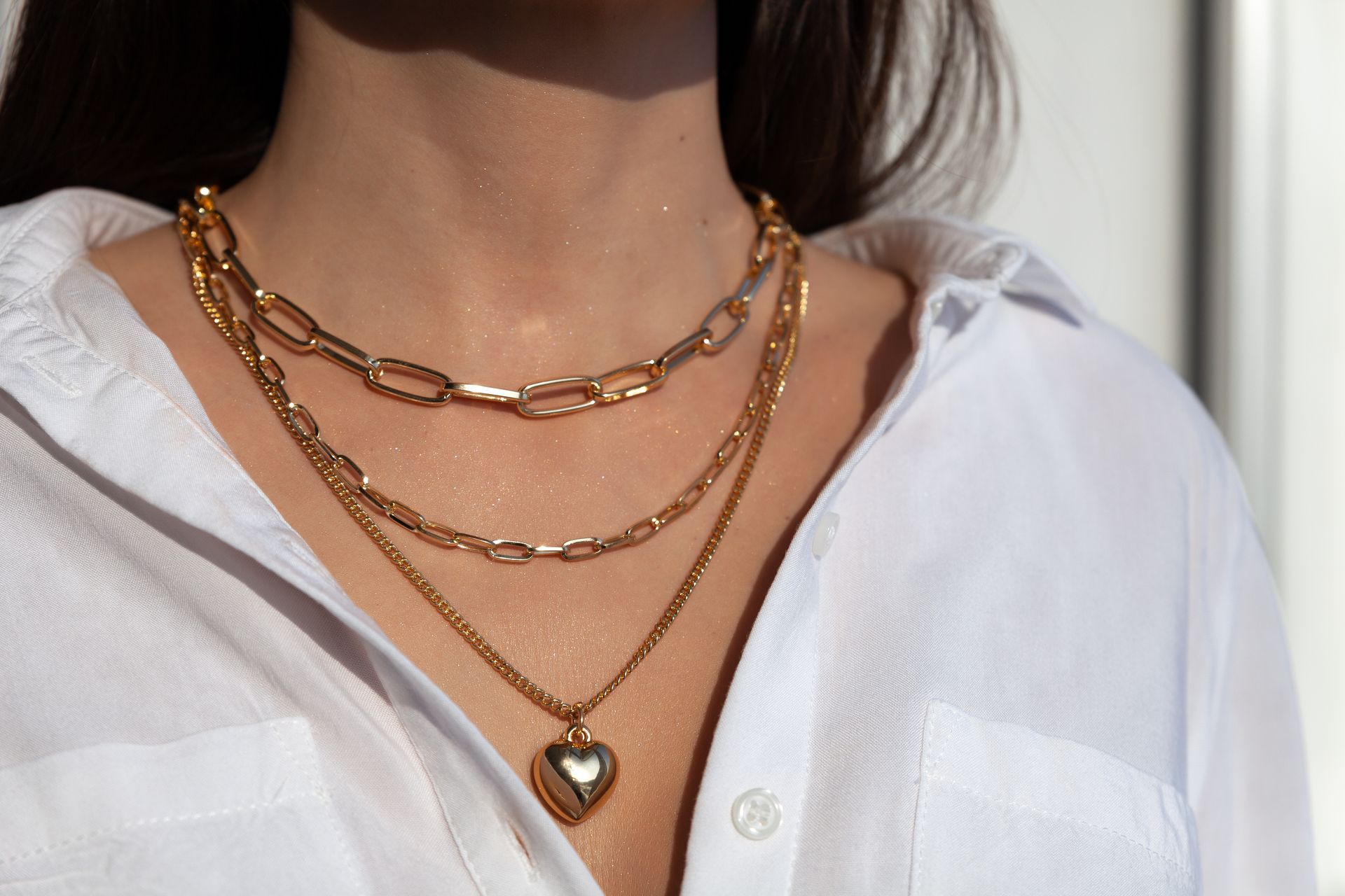 Gold layered necklaces over a white shirt, including a chain and a heart pendant