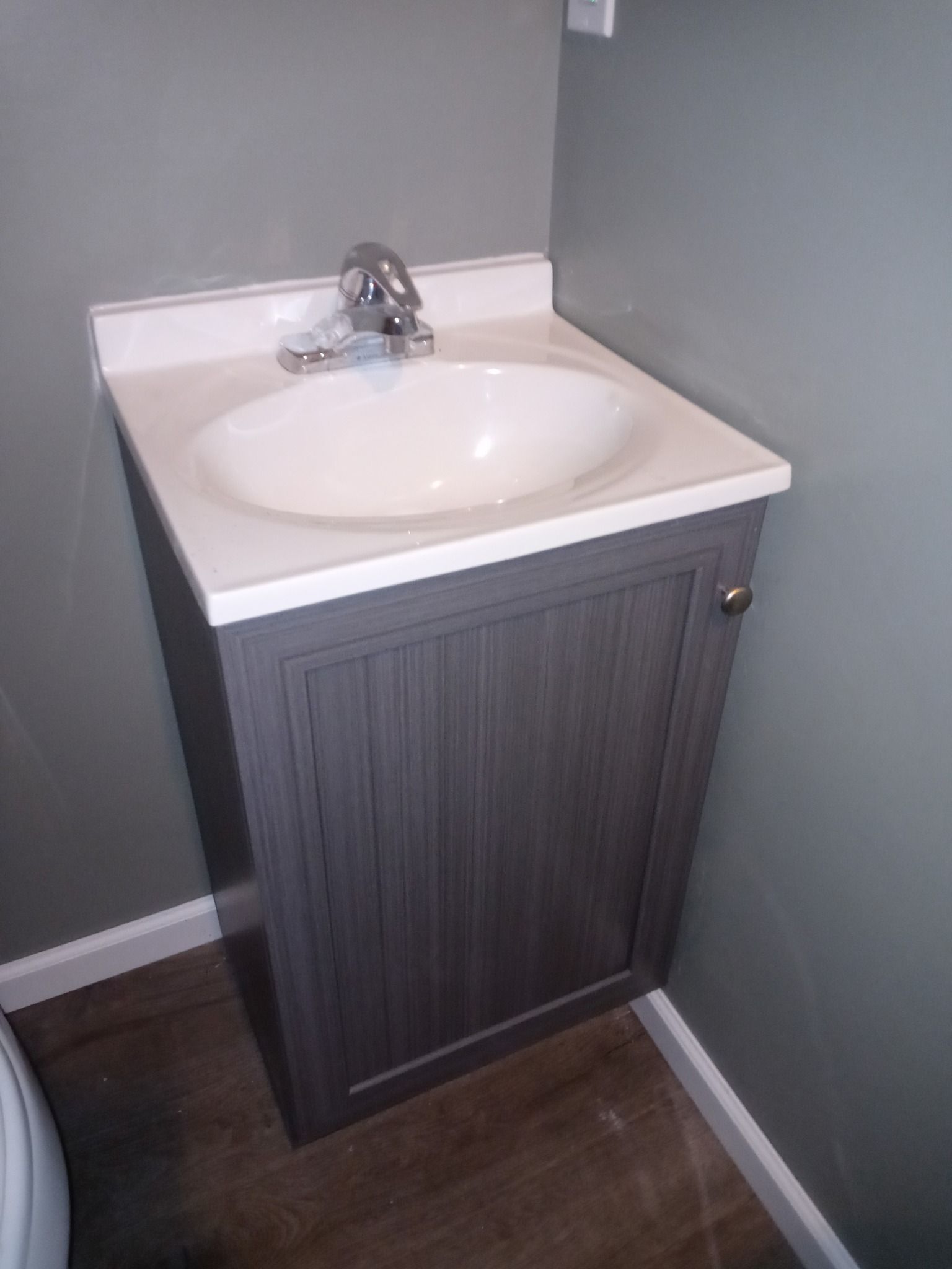 A grey bathroom vanity with a white sink and chrome faucet, set against grey walls and wood-look flooring.