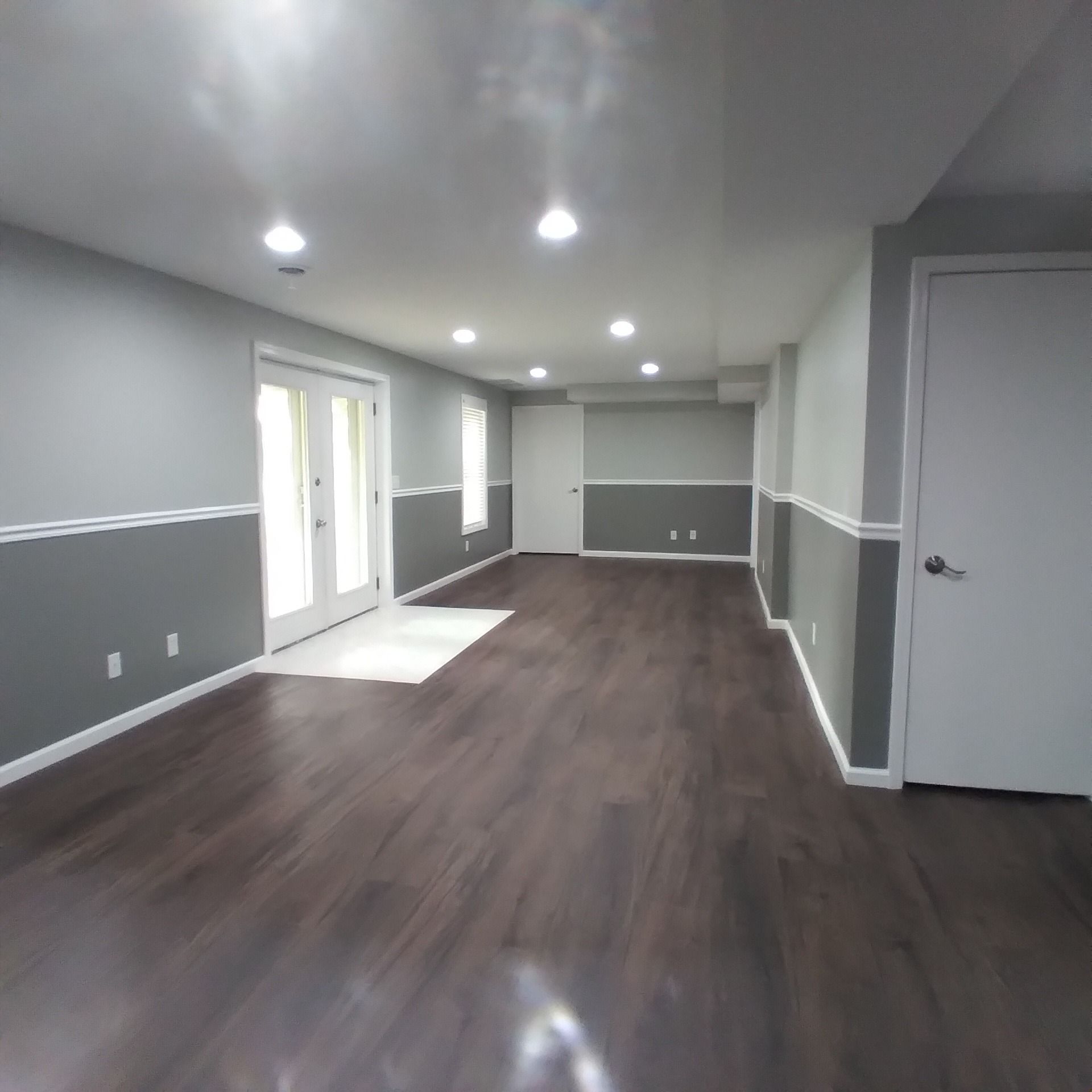 A finished basement with dark wood-look flooring, light grey upper walls, dark grey lower walls, and white trim.