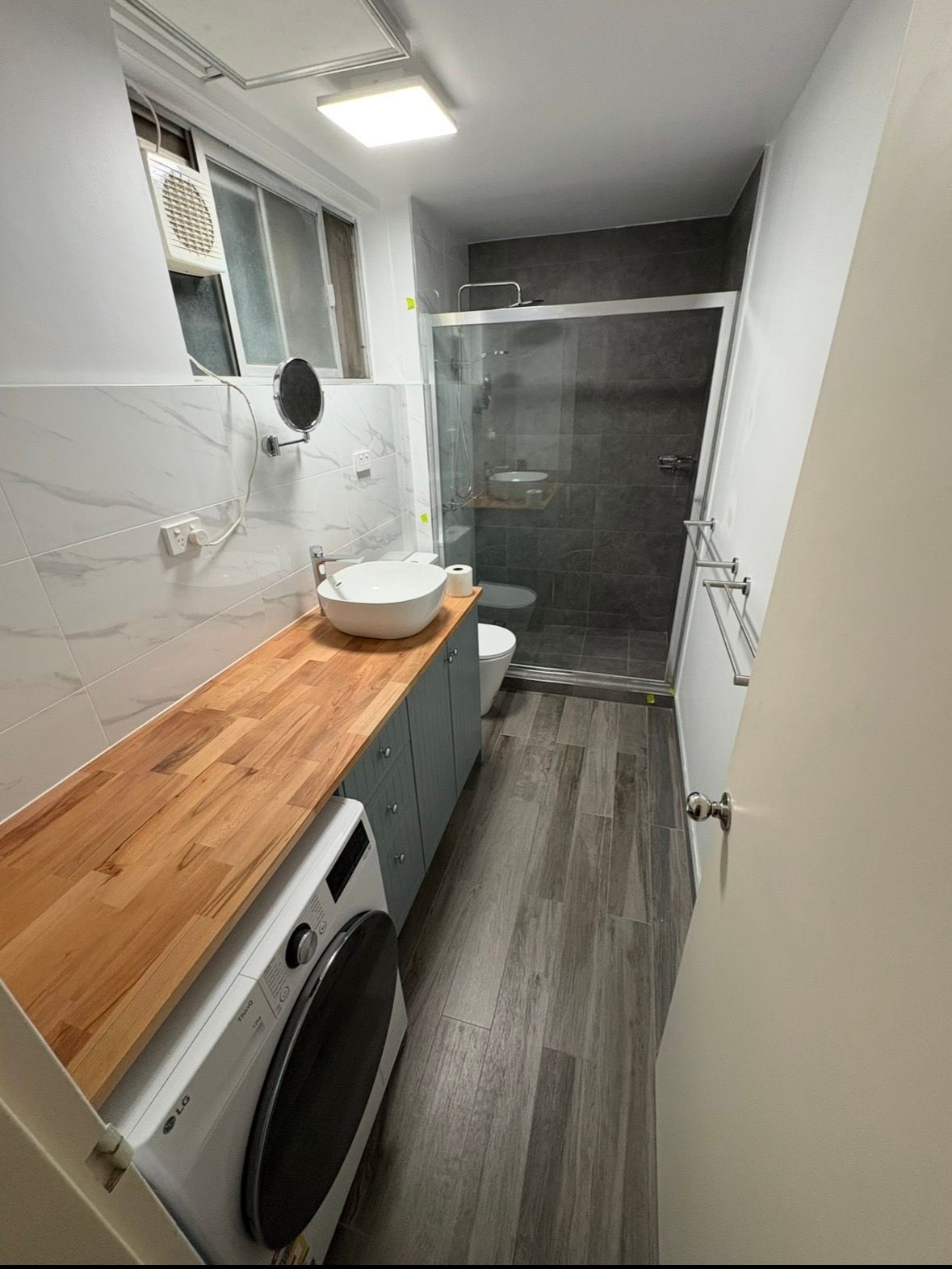 Narrow laundry room with wooden countertop, sink, washing machine, and dark door at the end.