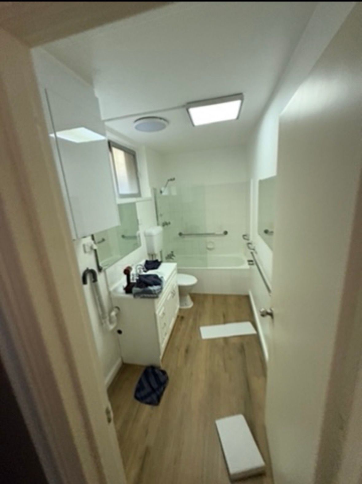 Small bathroom with tub, sink, toilet, and scattered items on the floor.
