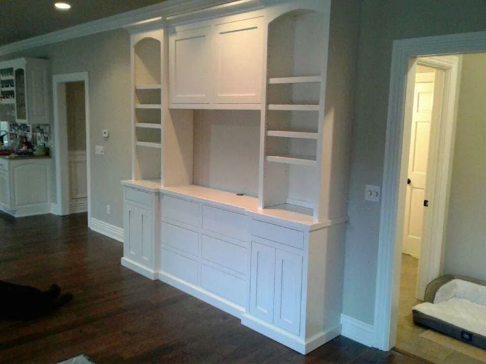Built-in white entertainment center in a living room with dark hardwood floors and an open doorway