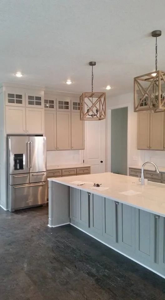 Bright modern kitchen with white island, stainless refrigerator, and hanging pendant lights