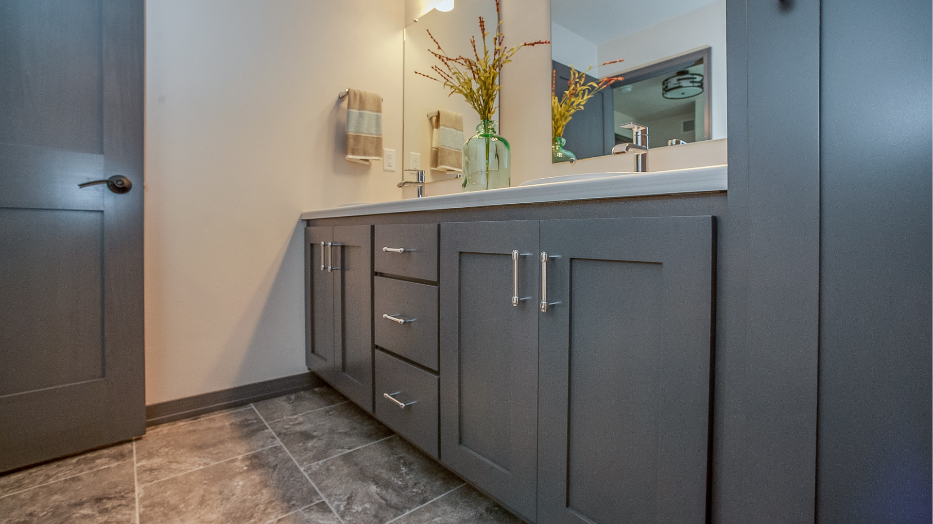 Modern bathroom vanity with gray cabinets, white countertop, mirror, and dark tile floor