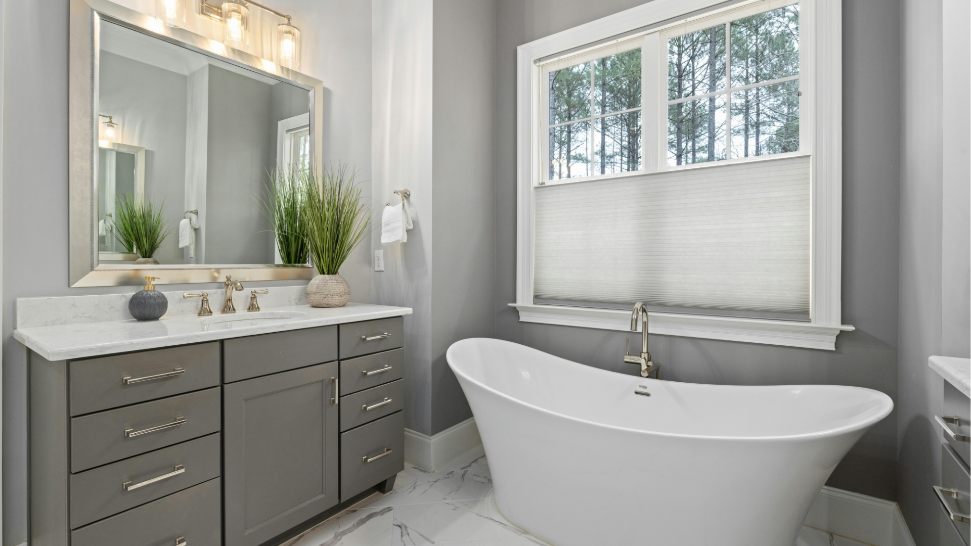 Bright modern bathroom with gray vanity, mirror lights, white tub, and window above the tub