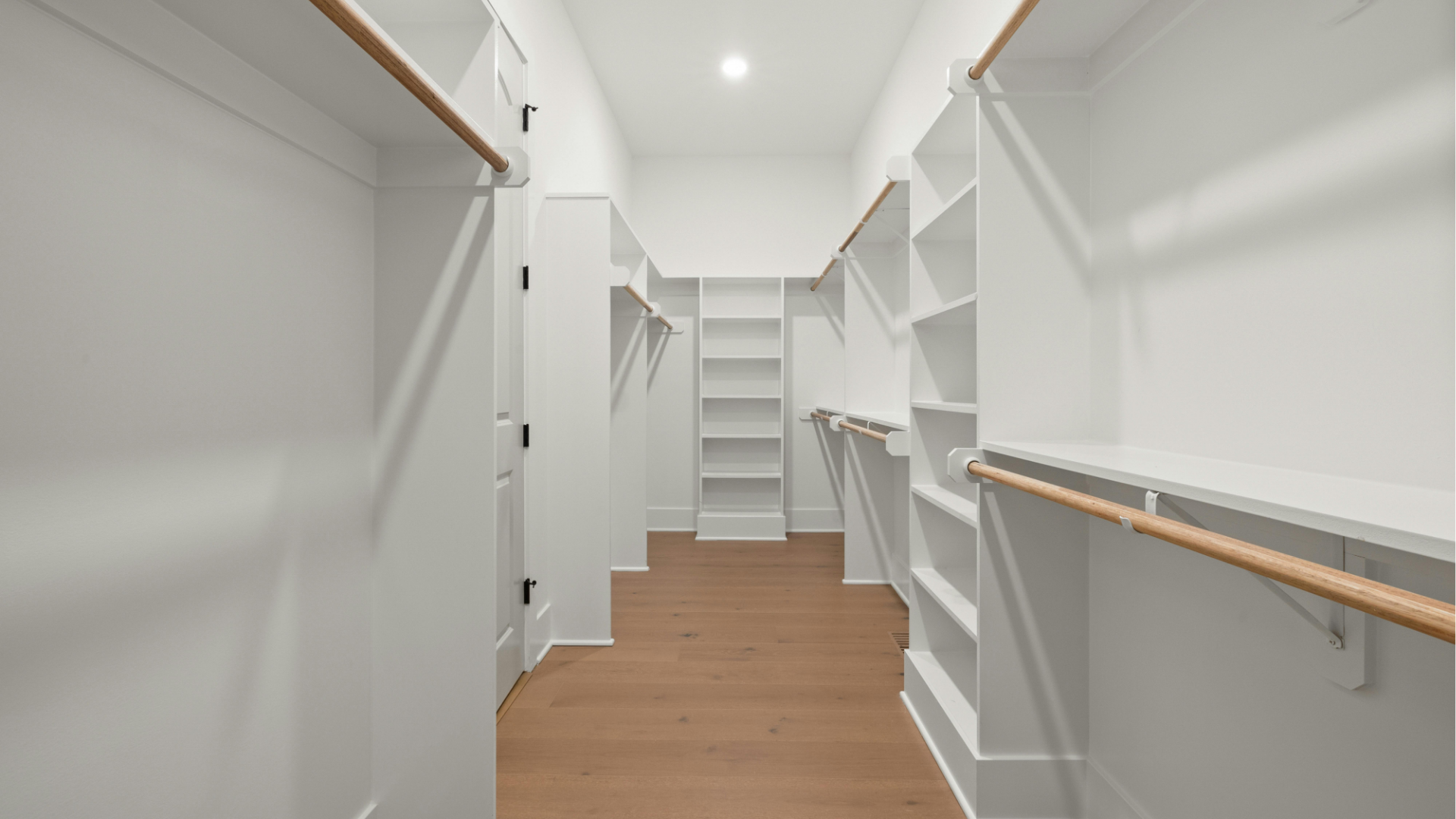 Bright walk-in closet with white shelves, hanging rods, and wood flooring
