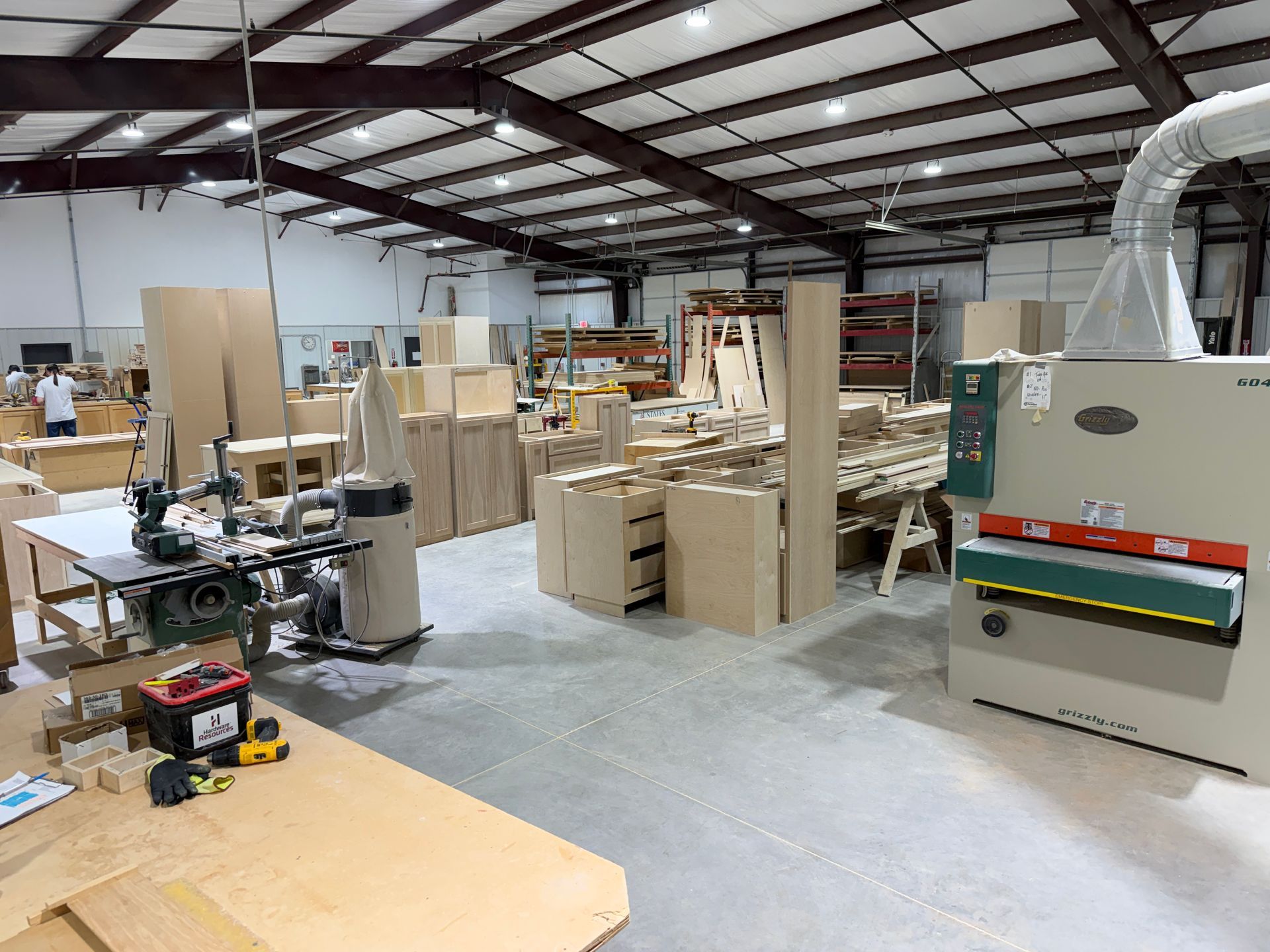 Large workshop with wood pieces, tools, and machinery under a metal-beam ceiling.