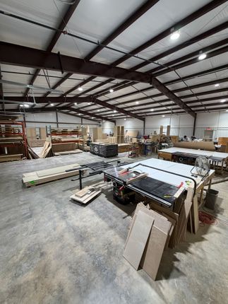 Large warehouse workshop with tables, tools, lumber, and materials under a metal beam ceiling.