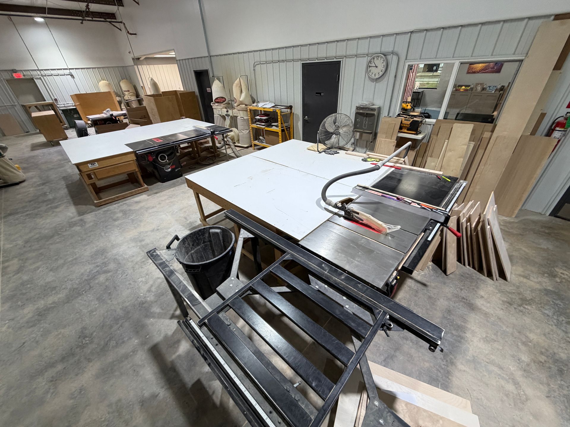 Woodworking shop with tables, shelves, tools, and a large workbench in the foreground