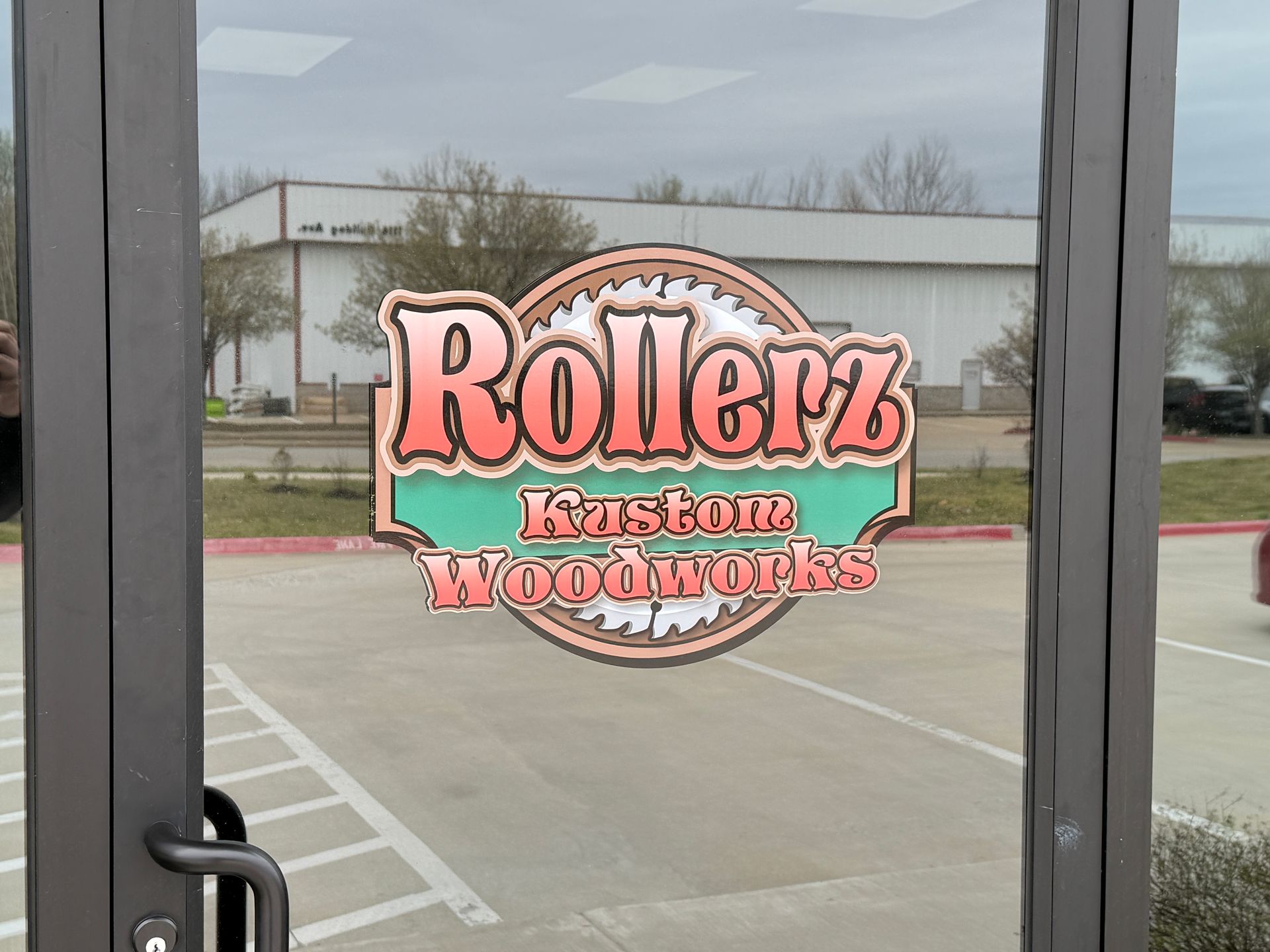 Rollerz Easton Woodworks sign seen through glass doors, with parking lot outside