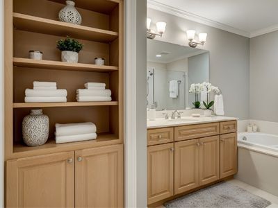 Bathroom vanity with wood cabinets, open shelving, folded towels, and a mirror above a white countertop