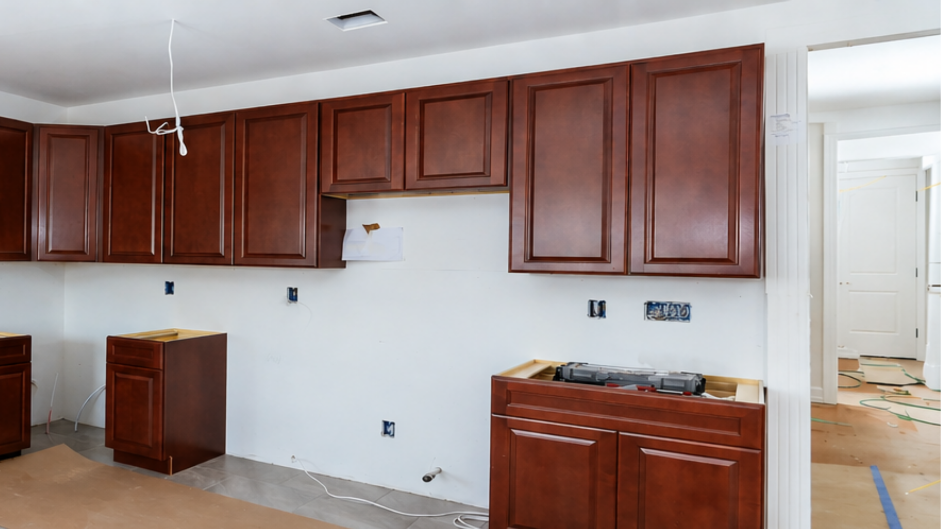 Partially renovated kitchen with cherry cabinets, white walls, and uncovered appliances under installation.