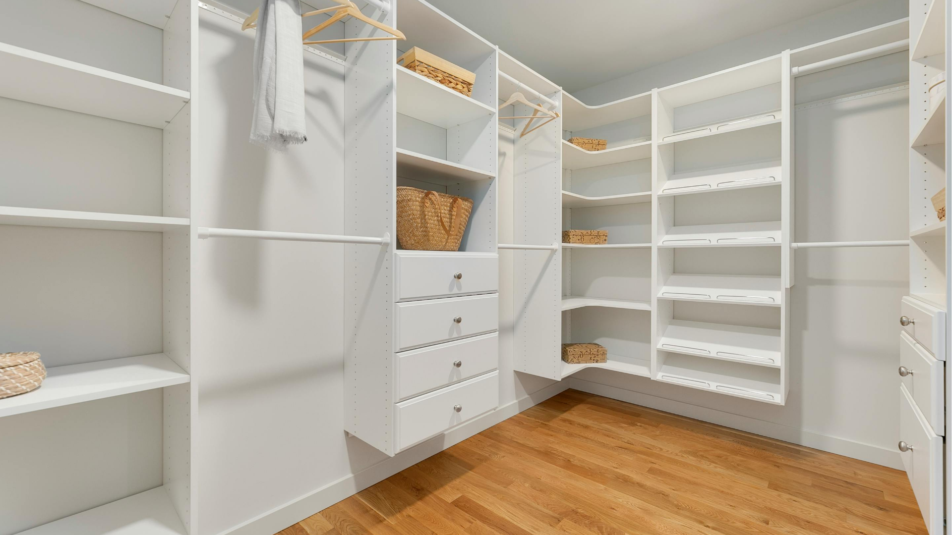 Walk-in closet with white shelving, hanging rods, drawers, and wood flooring