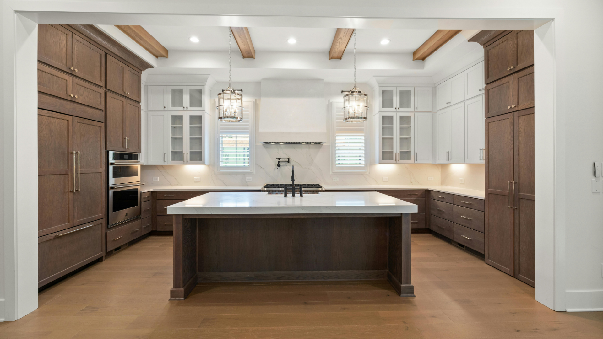 Modern kitchen with a large island, white cabinets, wood floors, and dark built-in appliances