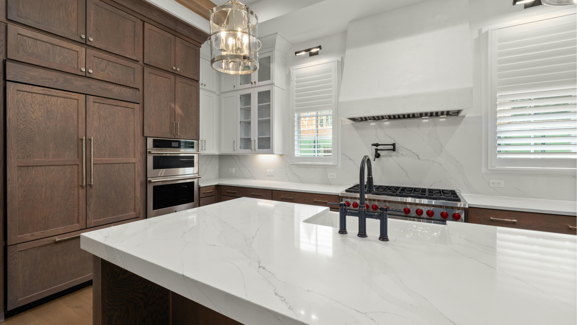 Modern kitchen with white island, wood cabinets, stainless appliances, and pendant lights.