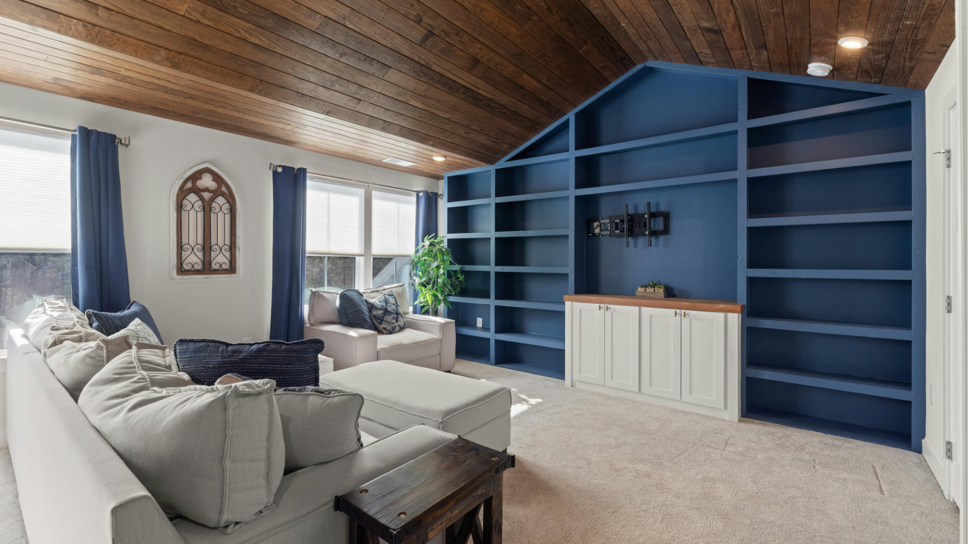 Bright living room with gray sofas, wood ceiling, large blue built-in shelves, and white cabinet.