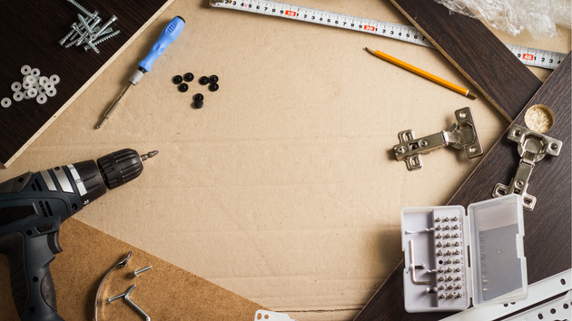 Workbench with drill, ruler, pencil, screws, and metal hardware around an empty cardboard workspace